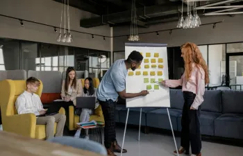 Unos jóvenes están en la oficina mientras que uno de sus compañeros están explicando en una pizarra