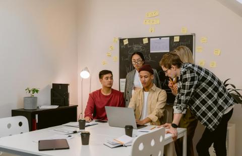 Un grupo de jóvenes están en una oficina viendo el ordenador de su compañero 