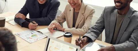 Un grupo de empresarios están sentado alrededor de una mesa en la que hay informes sobre datos y un ordenador