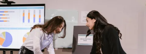 Unas trabajadoras están en un despacho analizando datos y gráficas en un una pantalla