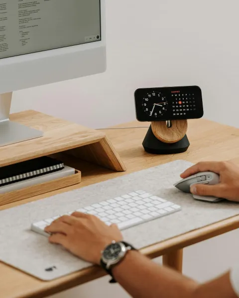 Una persona esá con su ordenador trabajando y encima de la mesa hay un reloj