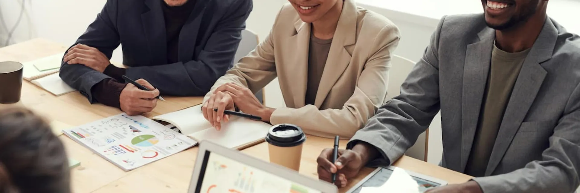 Un grupo de empresarios están sentado alrededor de una mesa en la que hay informes sobre datos y un ordenador