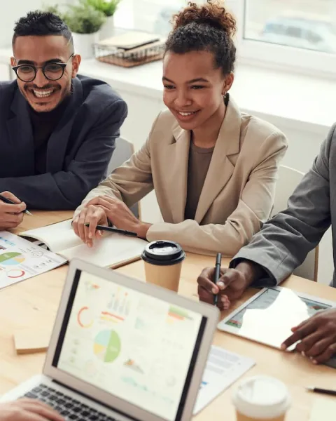 Un grupo de empresarios están sentado alrededor de una mesa en la que hay informes sobre datos y un ordenador